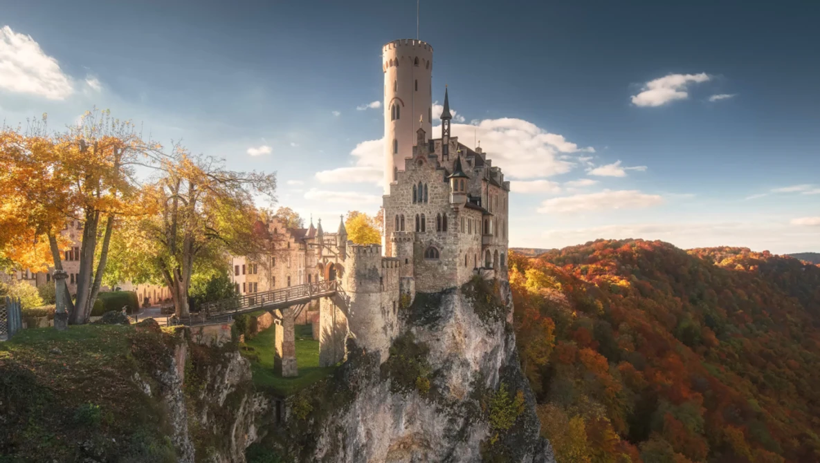 Medieval castle perched on a steep rocky cliff surrounded by autumn forest.