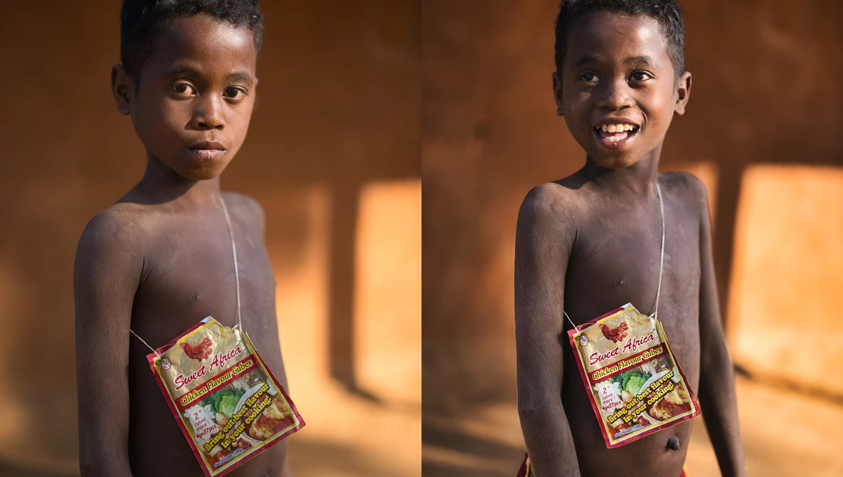Young child holding a packaged food item, smiling at camera in warm indoor lighting.