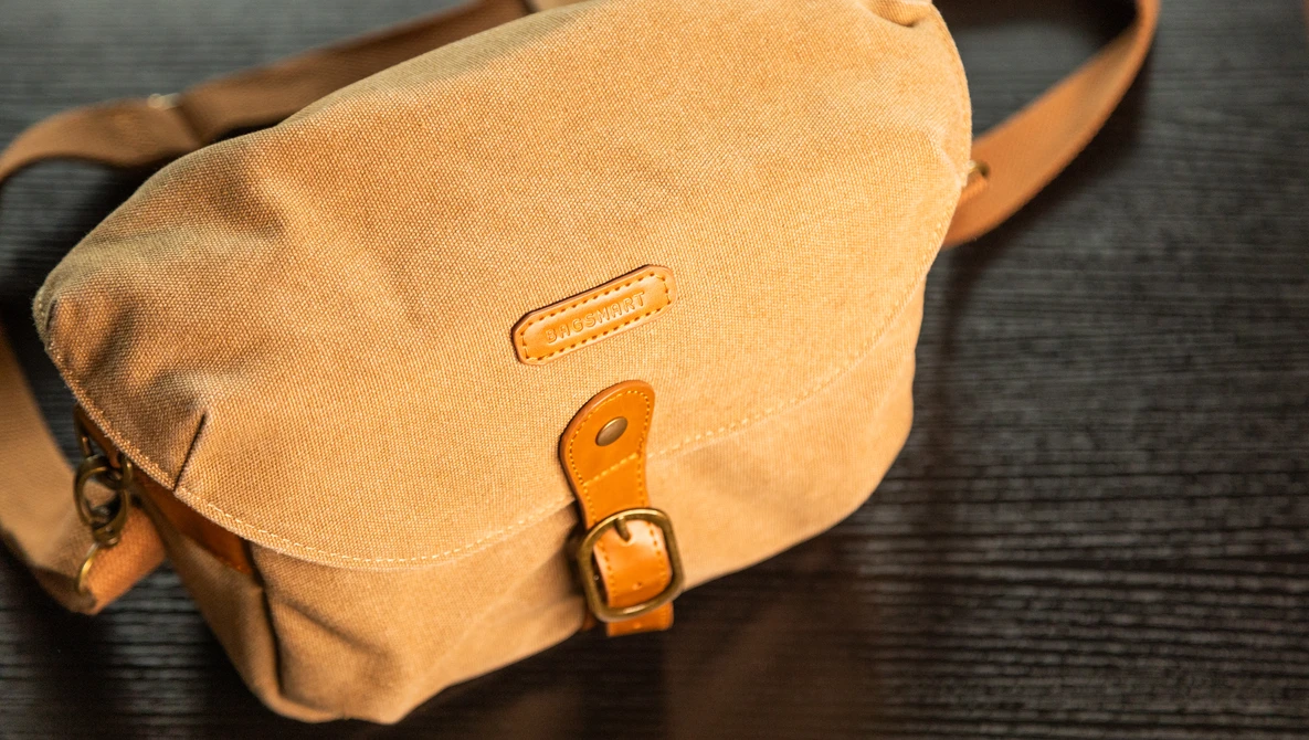 Tan leather messenger bag with brass buckle and shoulder strap on dark surface.