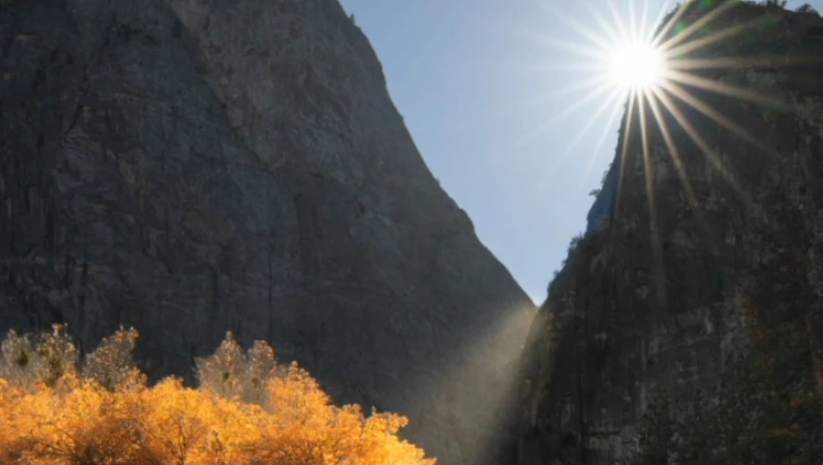 Sun streaming through a narrow mountain valley with golden autumn vegetation in the foreground and steep granite cliffs on both sides.