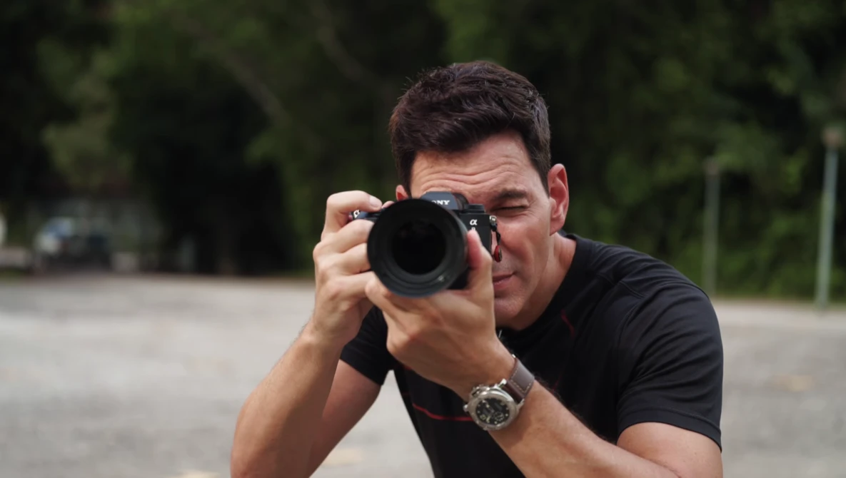 Male photographer holding a DSLR camera with telephoto lens, looking through the viewfinder.