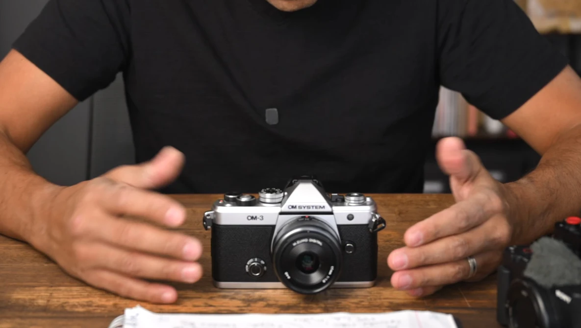 Hands presenting a vintage rangefinder camera on a wooden surface.