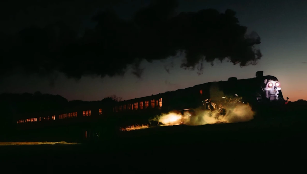 Steam locomotive at night with illuminated passenger cars and dramatic smoke plume against darkening sky.