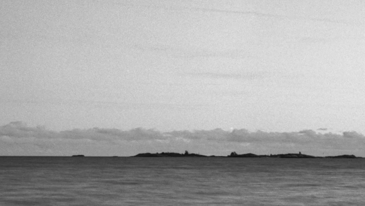 Minimalist black and white seascape with dark landmasses silhouetted against an overcast sky.