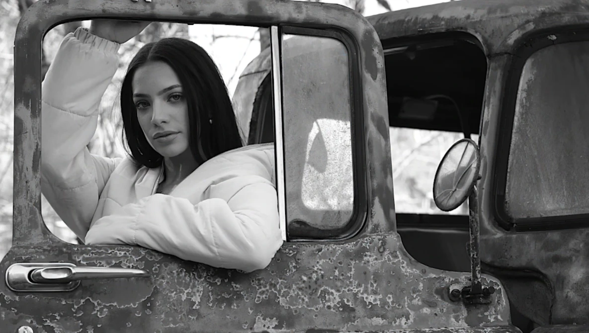 Woman in white jacket leaning out of vintage truck window in black and white portrait.