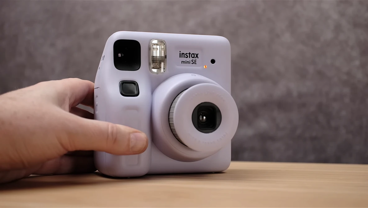 Lavender Instax Mini SE instant camera held in hand against neutral background.