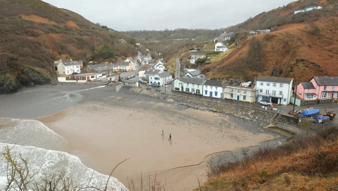 Coastal village nestled in a valley with sandy beach at low tide and residential buildings along the shoreline.