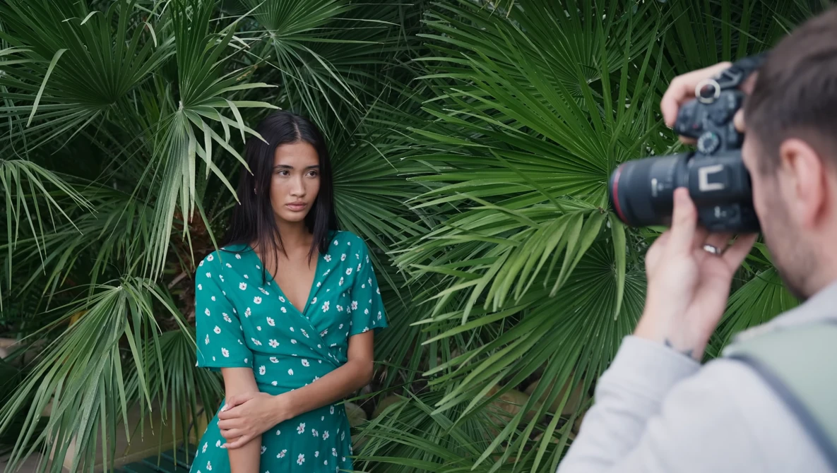 Portrait photographer shooting a woman posed against lush green palm fronds.