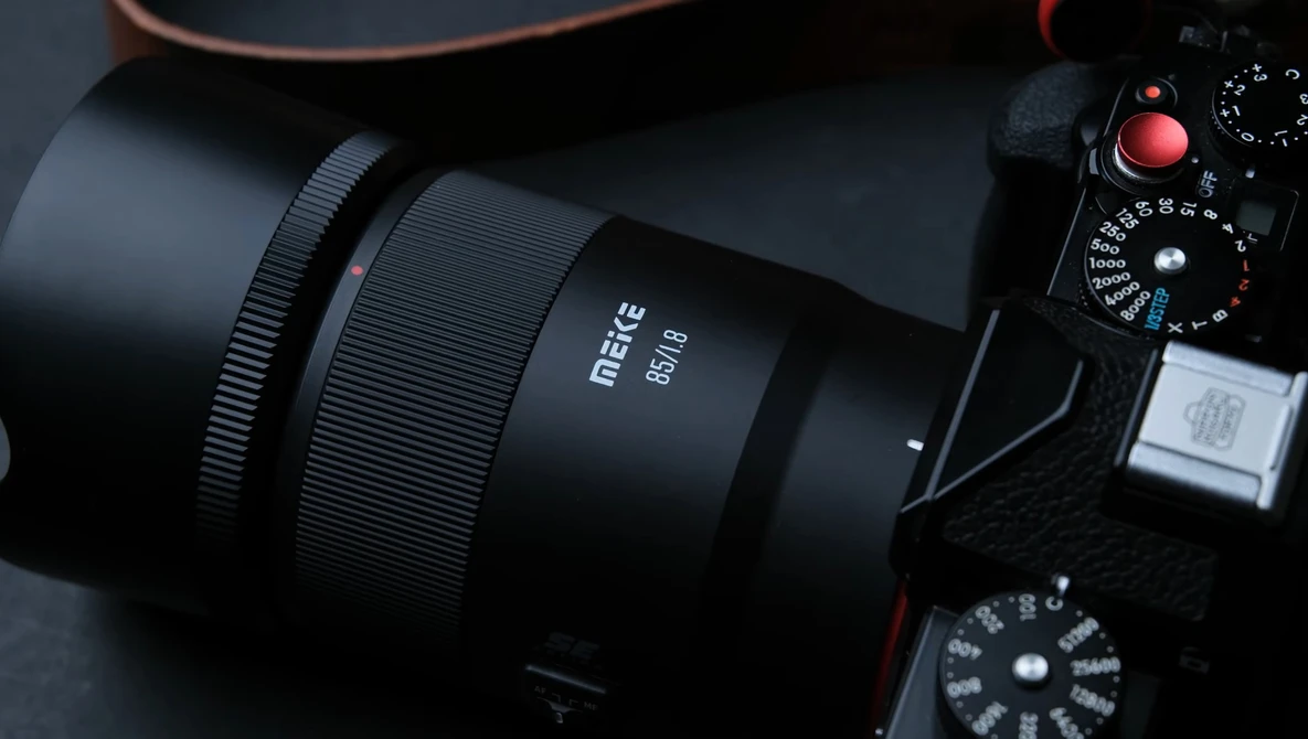 Matte black mirrorless camera with attached prime lens and visible control dials on dark surface.
