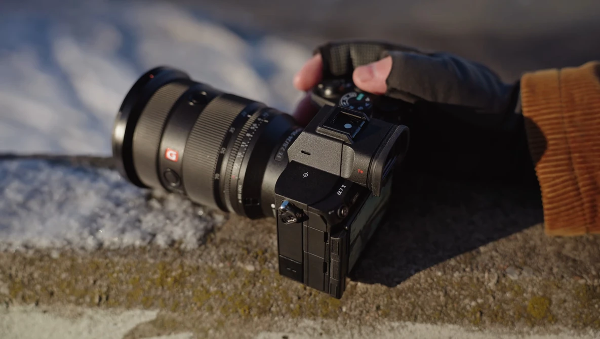 Mirrorless camera with wide-angle lens resting on sandy surface outdoors.