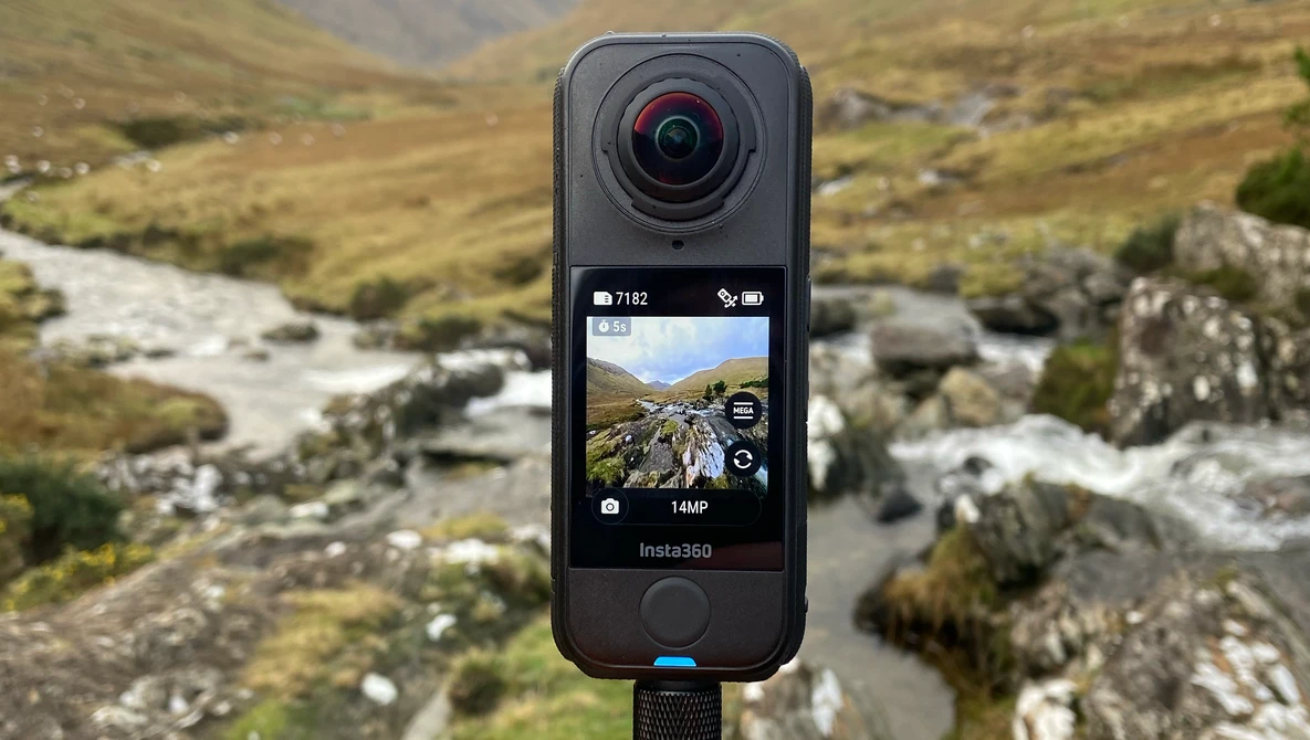 Insta360 action camera mounted on tripod displaying mountain stream landscape on rear screen.