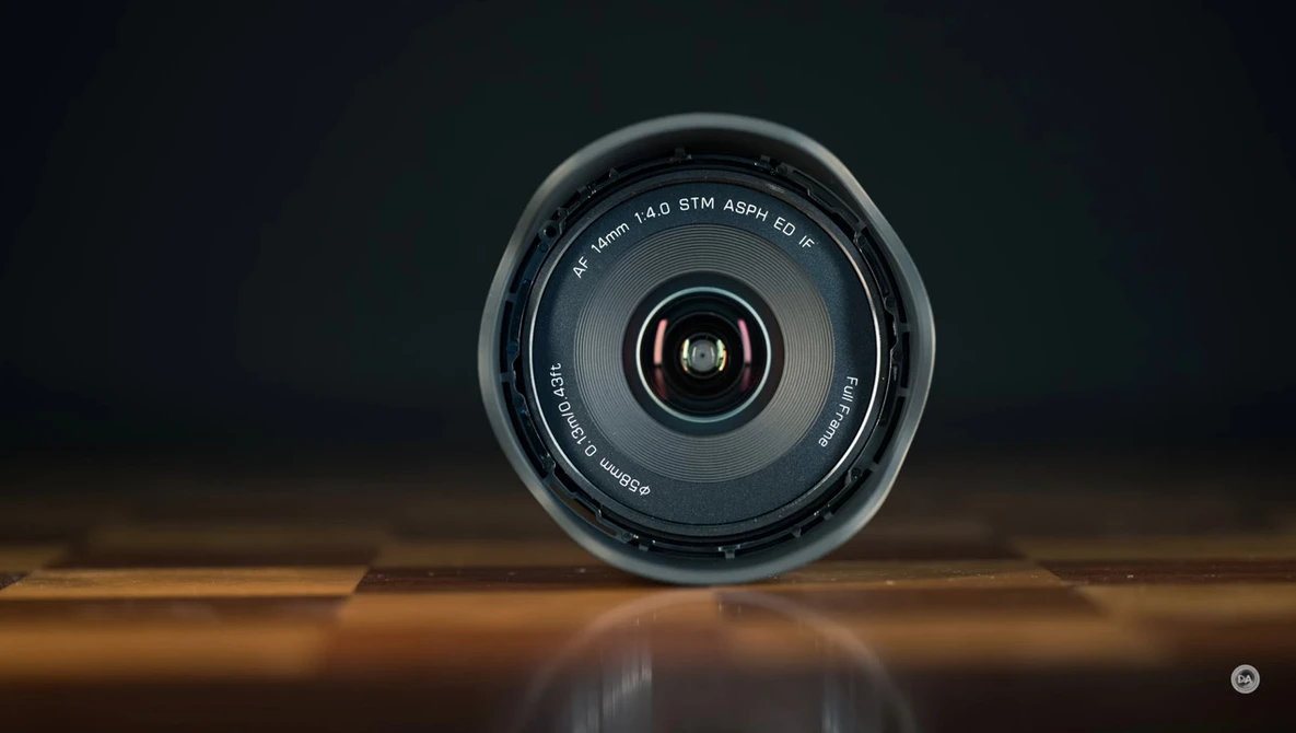 Camera lens viewed head-on against a dark background, positioned on a reflective wooden surface.
