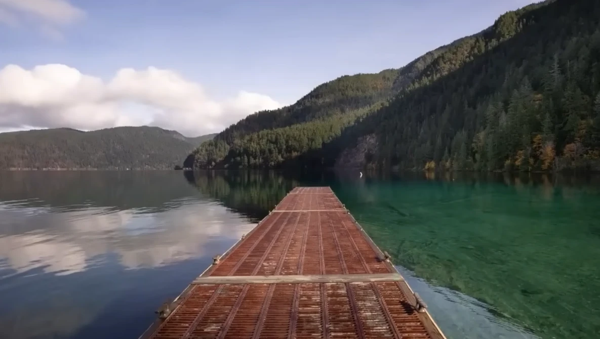 Wooden dock extending into a turquoise alpine lake surrounded by forested mountains.