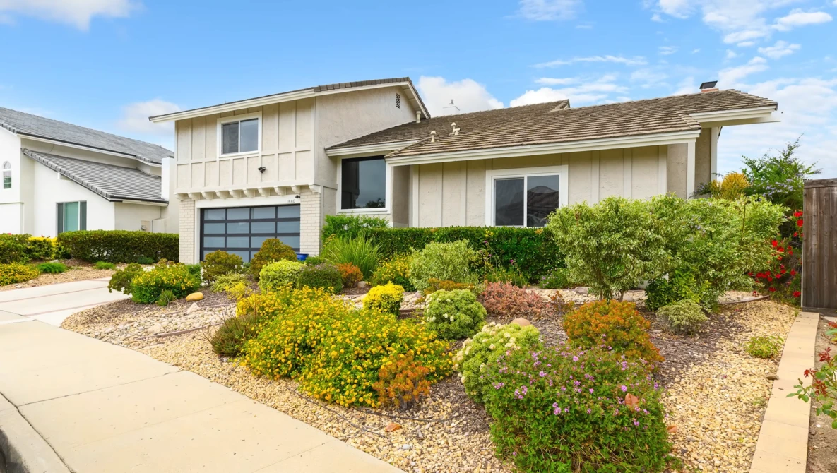 Contemporary two-story residential home with cream-colored siding, glass garage door, and drought-resistant landscaping.