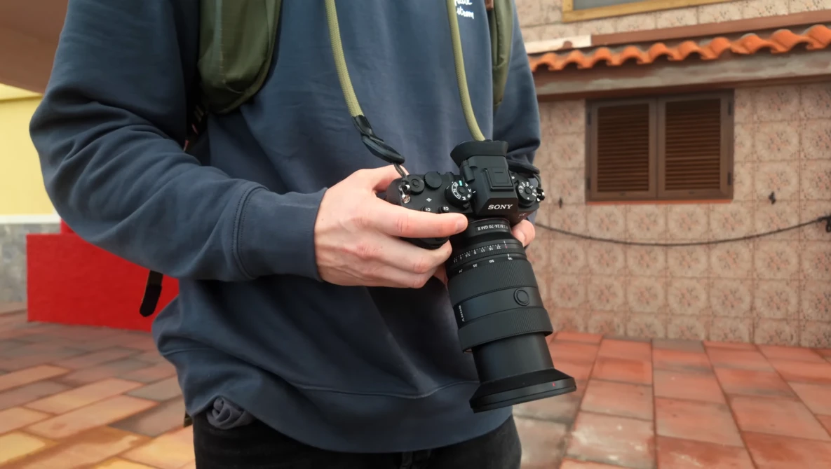 Photographer holding a Sony mirrorless camera with telephoto lens in an outdoor courtyard setting.
