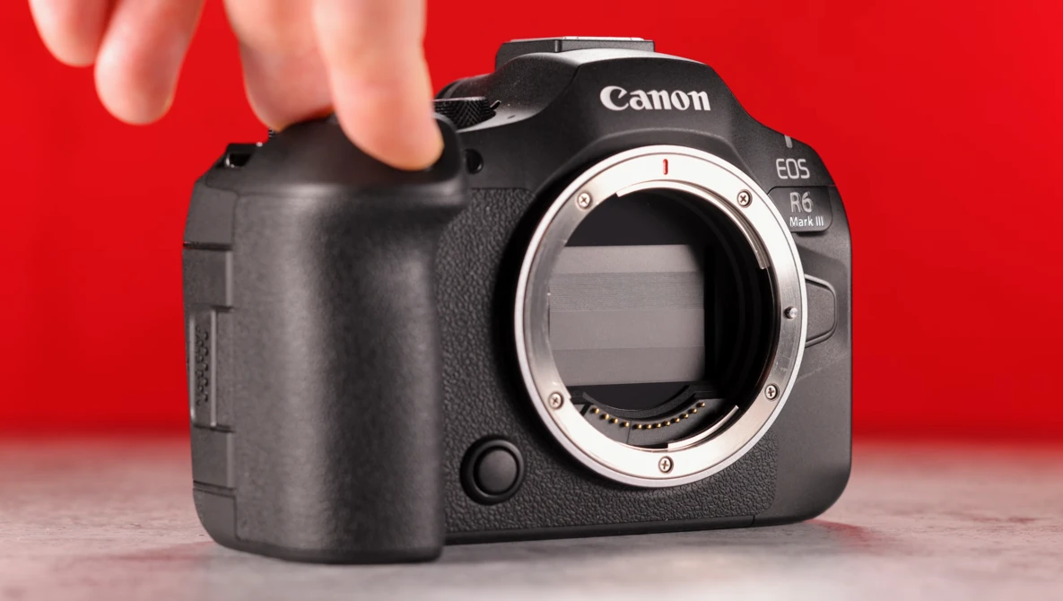 Canon EOS R6 Mark II mirrorless camera body held against red background, showing open mount without lens.