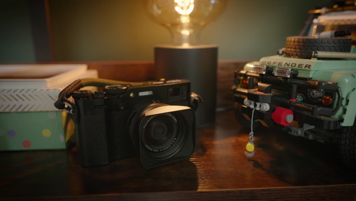 Black digital camera with lens displayed on wooden desk beside vintage sewing machines and warm lamp lighting.
