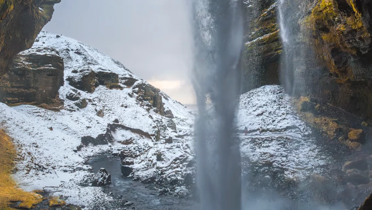 Tall waterfall cascading down snow-covered rocky cliffs with golden lichen visible on the stone.
