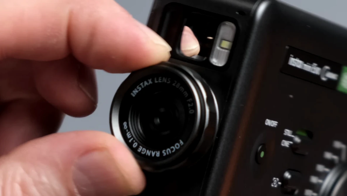 Hand holding a Fujifilm Instax instant camera with lens visible and flash unit mounted on top.