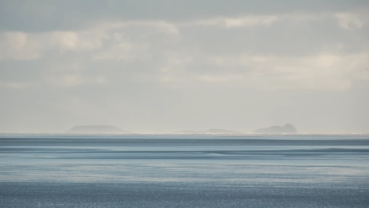 Calm seascape with distant headlands under overcast sky, horizontal layers of water and clouds.