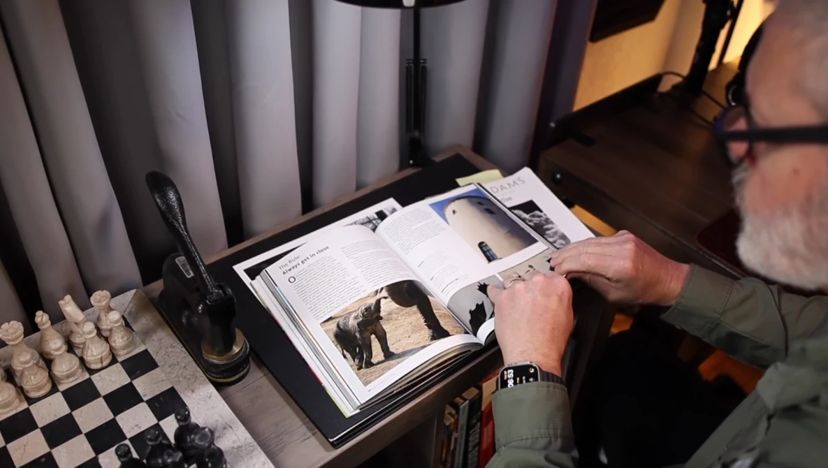 Photographer's hands holding open a printed portfolio or magazine on a desk next to a chess set.