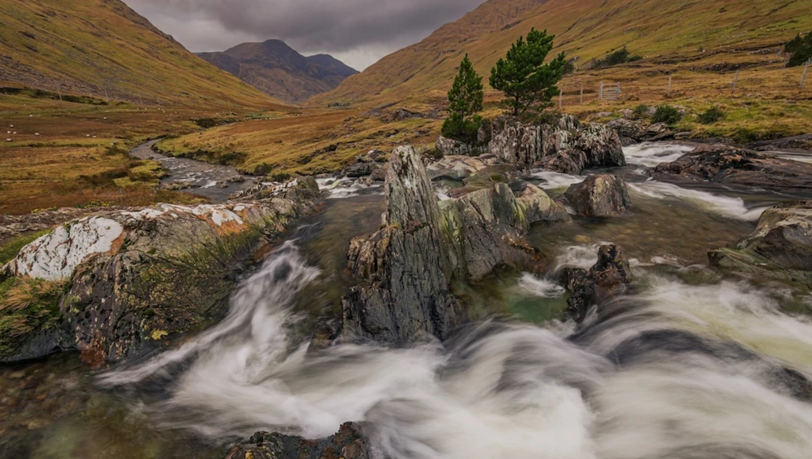 Mountain stream with smooth, flowing water cascading over layered rock formations in a misty valley.