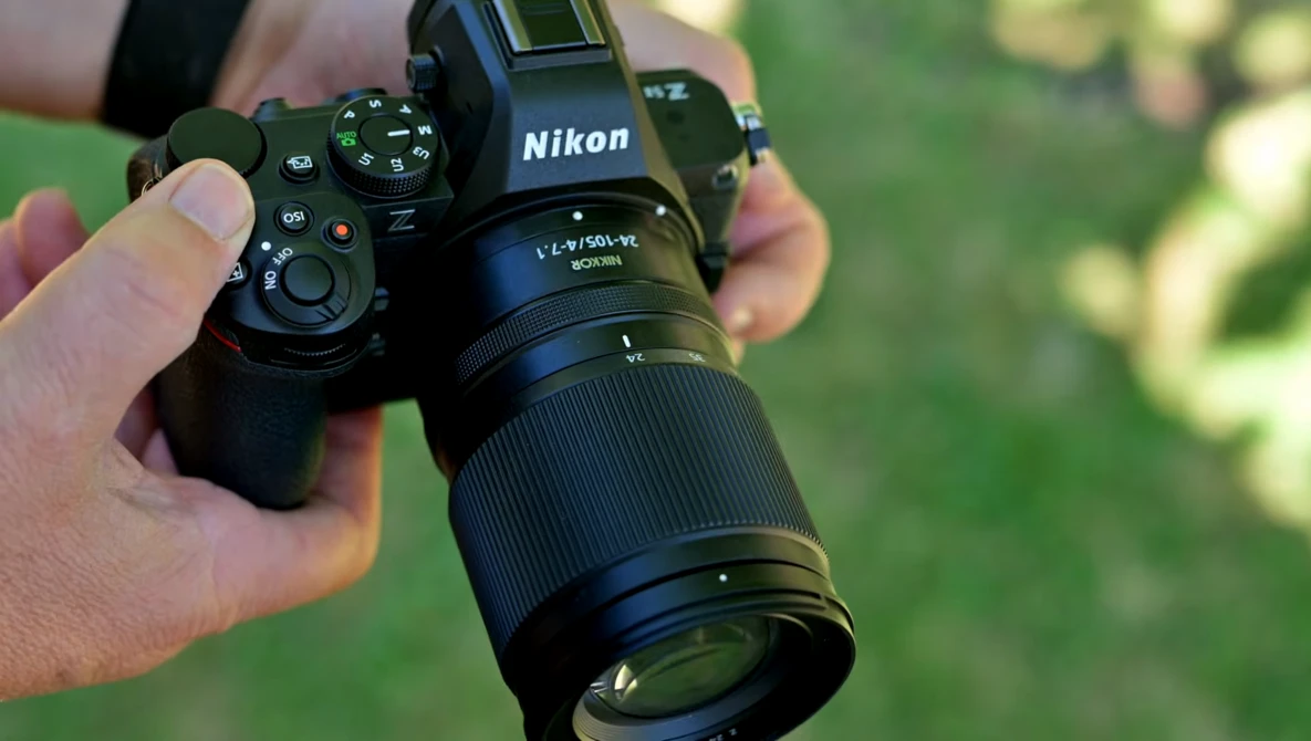 Photographer holding a Nikon mirrorless camera with telephoto lens against a blurred green background.