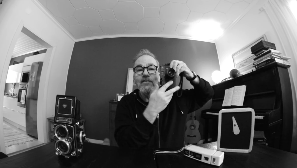 Photographer holding a rangefinder camera in a black and white self-portrait taken with a wide-angle lens.