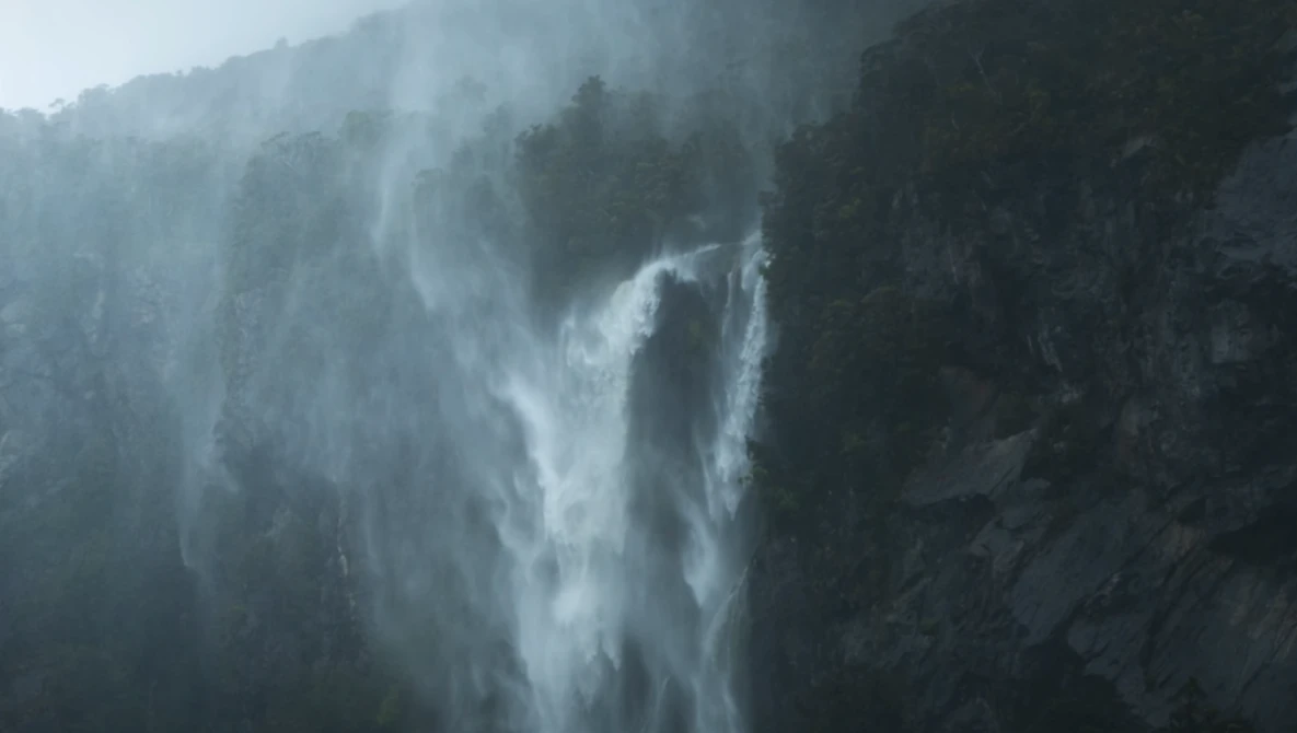 Misty waterfall cascading down a forested mountainside shrouded in fog.