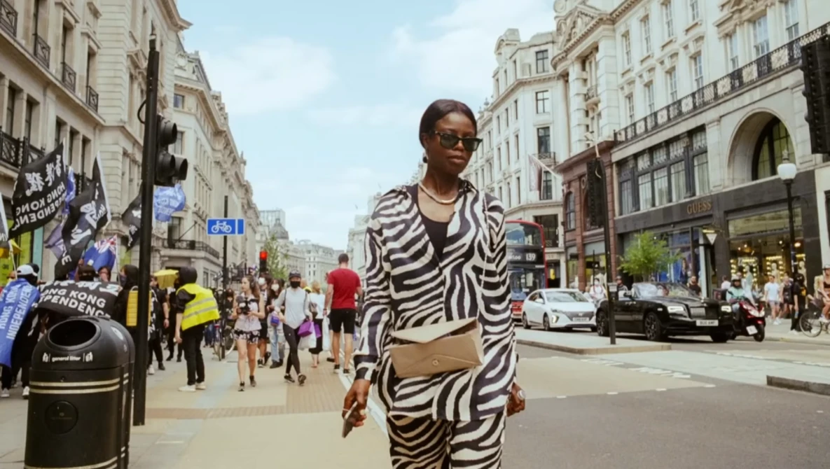 Woman in zebra-striped outfit walking on busy urban street lined with classical buildings.