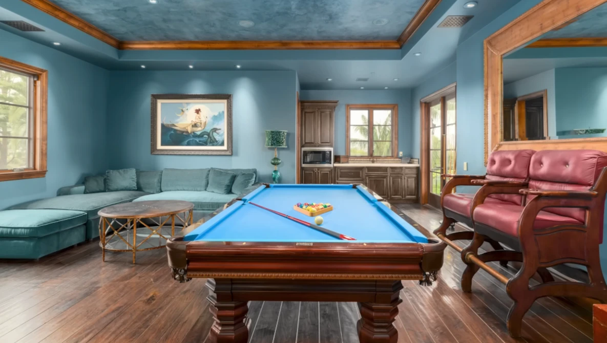 Billiards table with blue felt in a turquoise recreation room with wood ceiling beams.