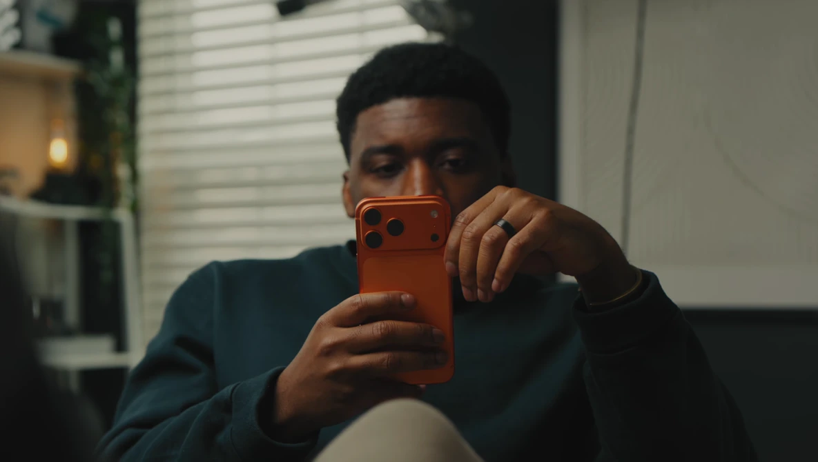 Man holding an orange smartphone up to his face while looking at the screen.