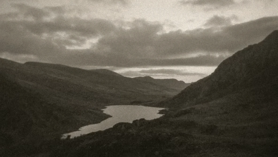 Mountain valley landscape with winding river and dramatic cloudy sky in monochrome.