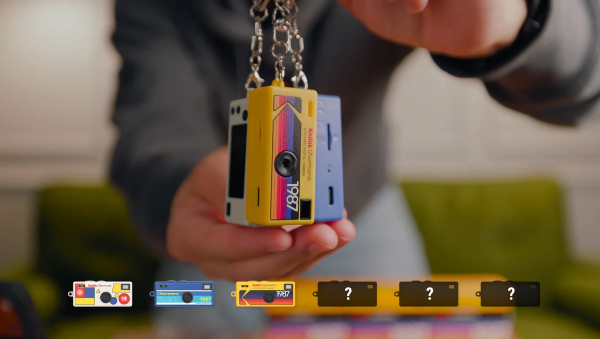 Person holding a yellow and pink instant camera pendant on a chain.