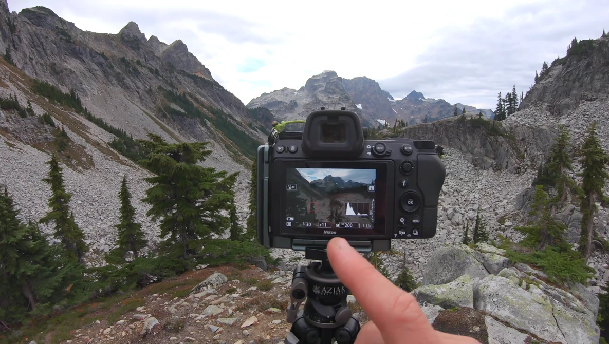 Camera mounted on tripod displaying mountain valley landscape on its rear screen.