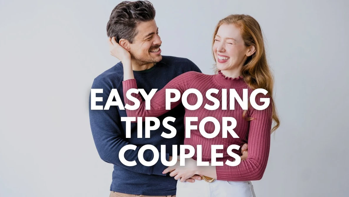 A man and woman smile at each other while posing together against a light gray background.
