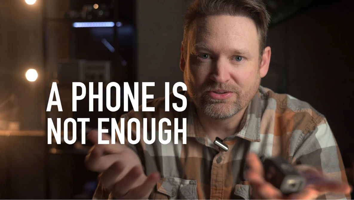 Man in plaid shirt gesturing while speaking, with text overlay reading "A PHONE IS NOT ENOUGH."