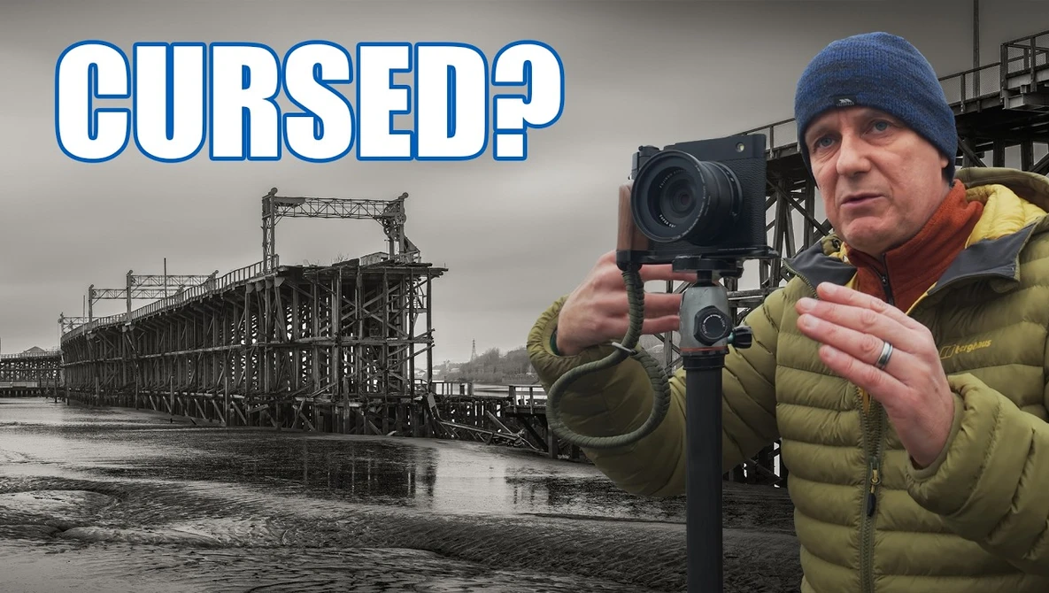 Photographer with camera and light meter standing before abandoned industrial steel structure.