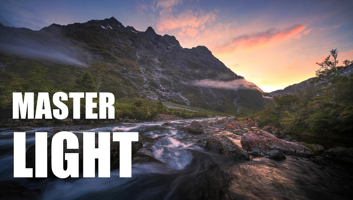 Mountain landscape at sunset with a flowing river in the foreground and dramatic sky.