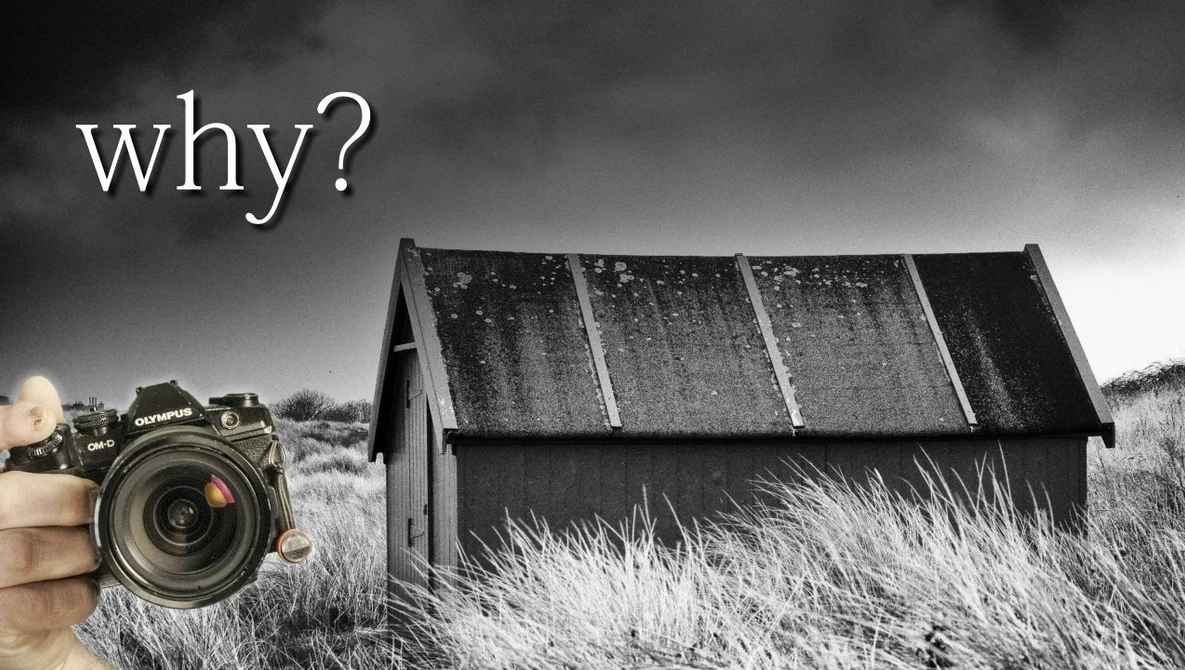 Photographer holding a DSLR camera pointed at a derelict house with solar panels in an overgrown field.