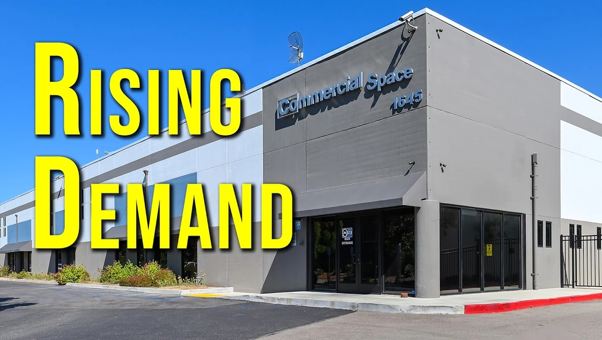 Modern industrial building with large storefront and yellow text overlay reading 'Rising Demand' against clear blue sky.