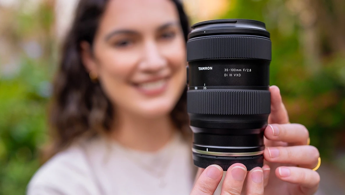 Person holding a Tamron 24-105mm f/2.8 telephoto lens toward the camera in an outdoor setting.
