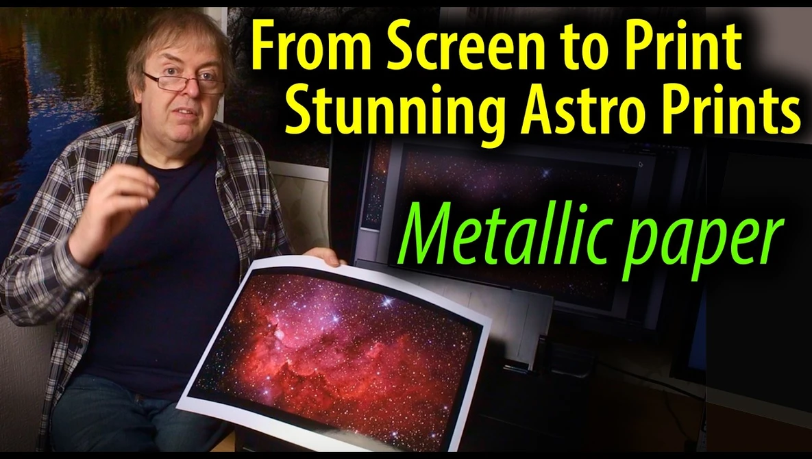 Man holding a metallically-printed astrophotography image showing a vibrant red and pink nebula with stars.