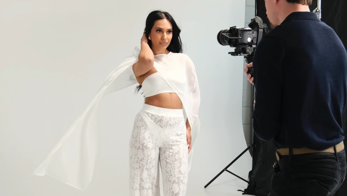 Model in white crop top and patterned pants poses during studio photoshoot with camera operator