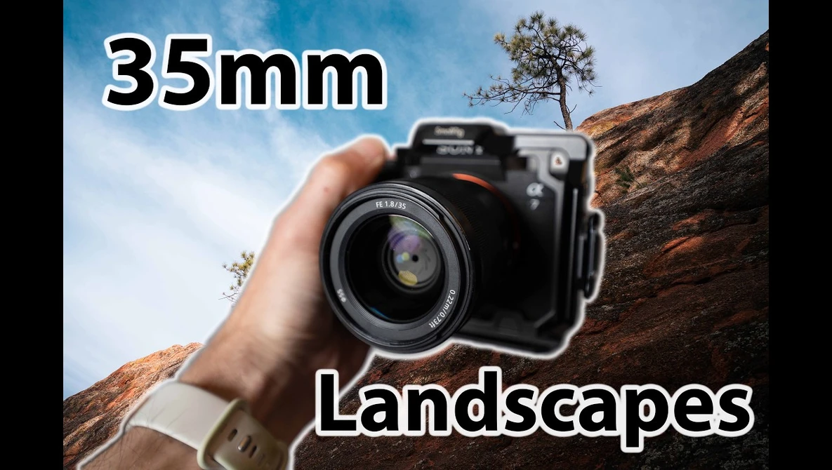 Hand holding a camera with a 35mm lens pointed at a rocky landscape with sparse vegetation.