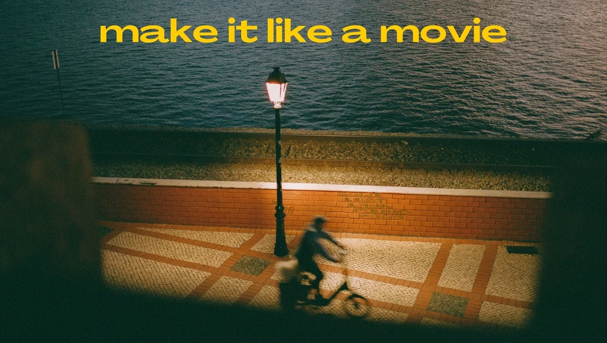 Person sitting on a waterfront boardwalk at dusk beneath a lit street lamp, with calm water and a brick seawall behind them.