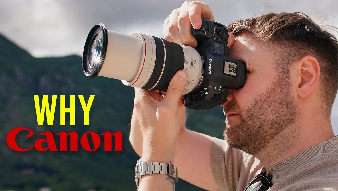 Photographer holding Canon telephoto lens to eye while composing a shot outdoors.