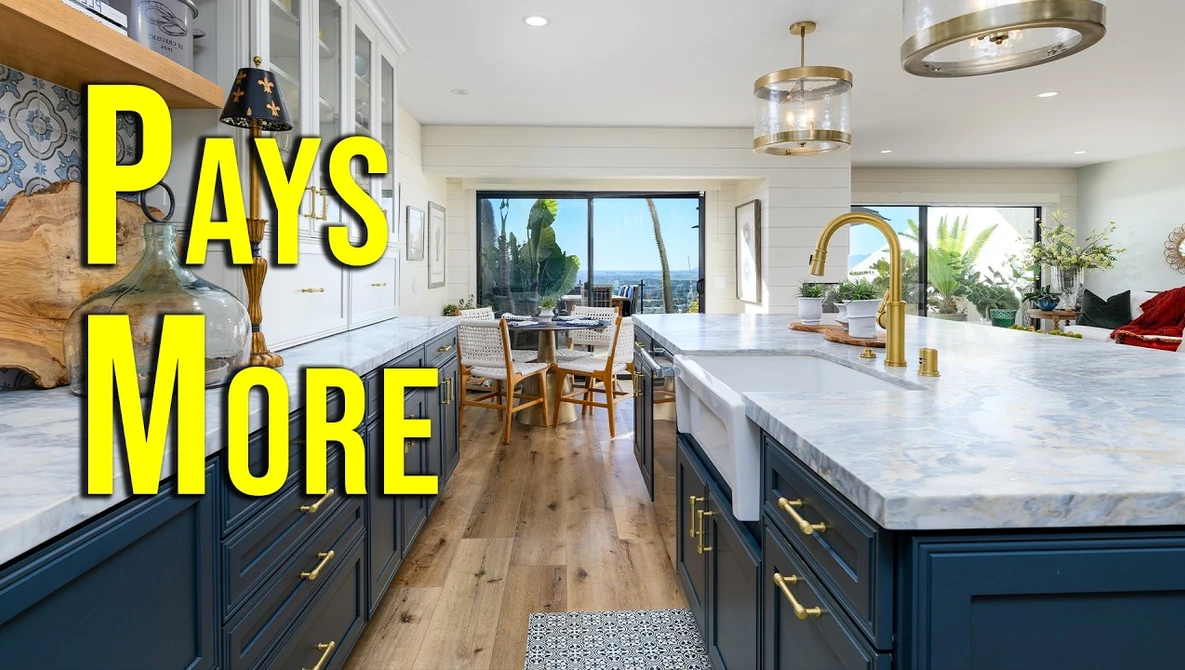 Modern kitchen with marble island countertop, dark blue cabinetry, and brass fixtures overlooking coastal views.