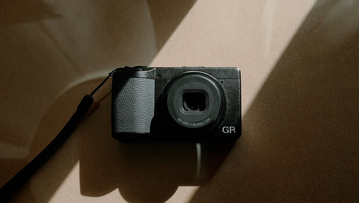 Ricoh GR compact digital camera viewed from above with natural window light casting shadows.