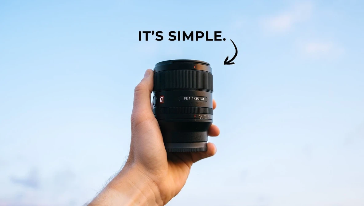 Hand holding a black telephoto lens against a blue sky background.